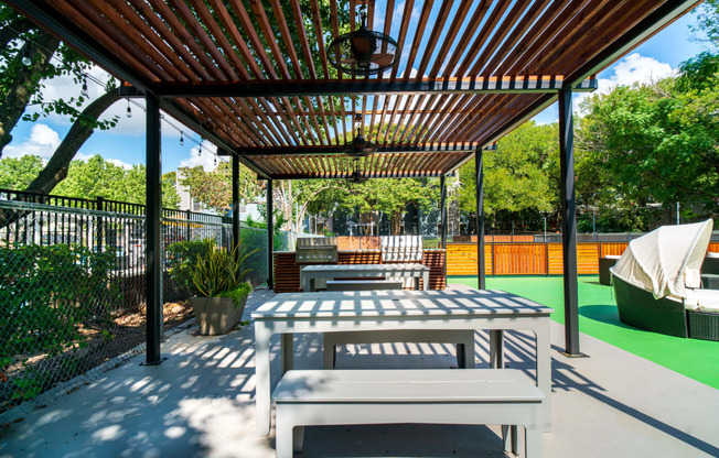 a patio with a picnic table and benches under a wooden trellis