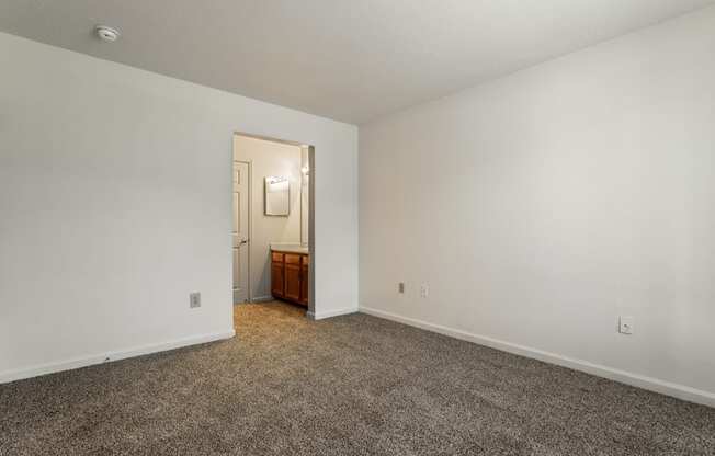 an empty living room with carpet and a door to a bathroom at Pheasant Run in Lafayette, IN 47909