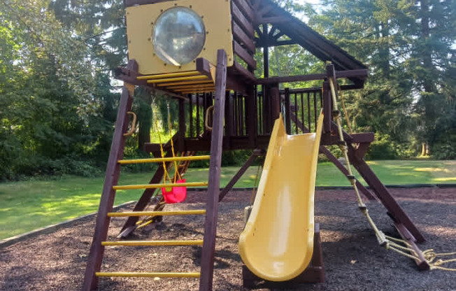 A playground with a yellow slide and a brown roof.
