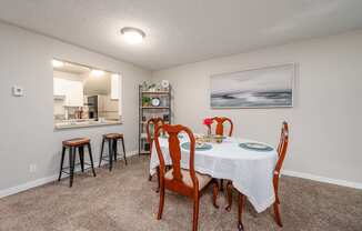 A dining room with a table set for two and a painting on the wall.