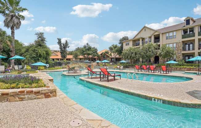 a swimming pool with chairs and umbrellas in front of an apartment building at The Verandah, Austin, TX