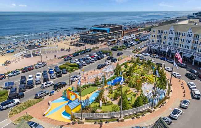 A view of a beachfront area with a playground, parking lot, and buildings.