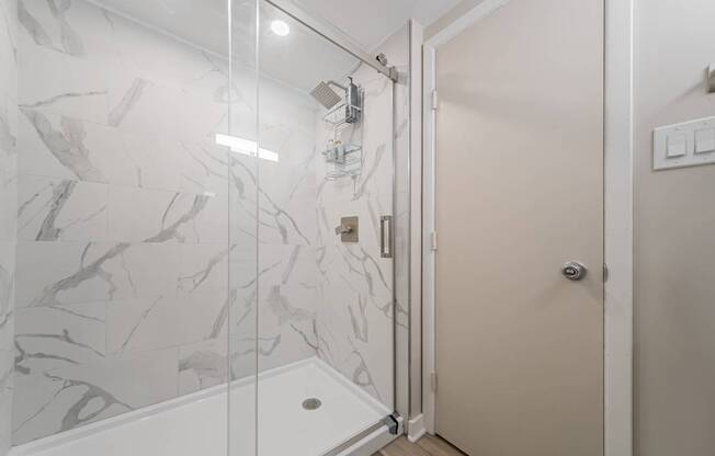 A white bathroom with a marble wall and a glass shower door.