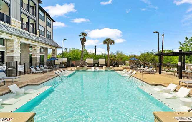 A large swimming pool with lounge chairs and palm trees in the background.