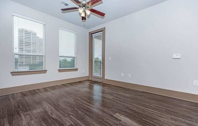 an empty living room with a ceiling fan and windows