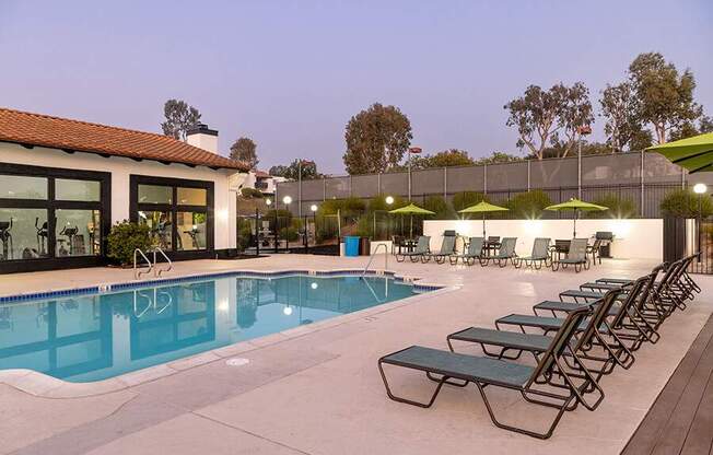 A pool with sun loungers and umbrellas in front of a building.
