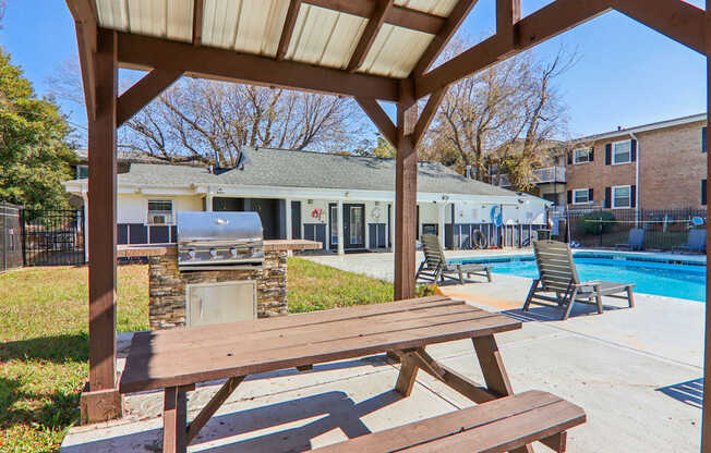 A wooden picnic table is in the foreground of a pool area.