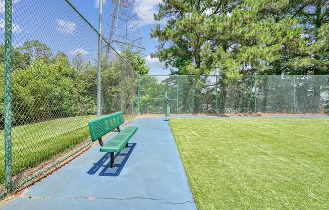 A green bench sits on a blue surface in a fenced-in area.