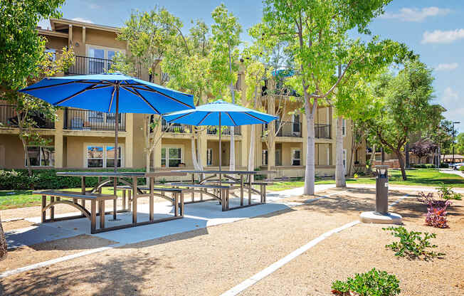 a picnic area with benches tables and umbrellas in front of an apartment building