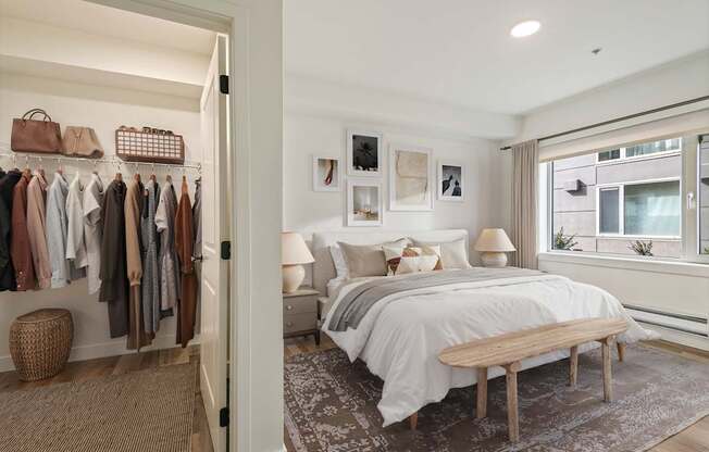 A bedroom with a bed, a bench, and a closet with clothes.