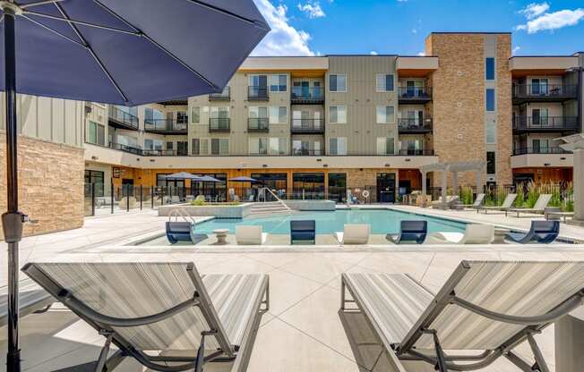 a pool with lounge chairs and umbrellas in front of a building