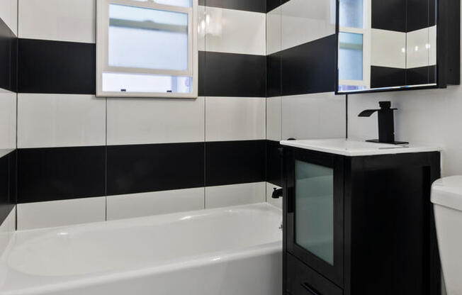 A black and white bathroom with a white toilet and a black cabinet at Brookmore Apartments Pasadena.