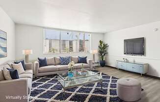 A living room with a glass coffee table and a large window.