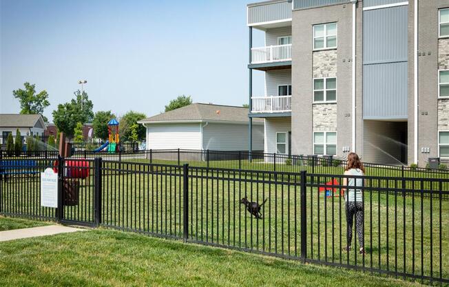 a girl is standing in a yard with a dog behind a fence