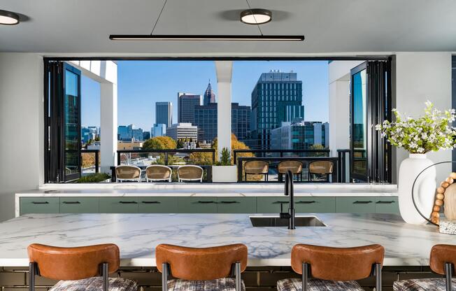 A shared kitchen and bar at Modera Westside Trail with expansive windows, skyline views, and seating designed for larger gatherings at home.
