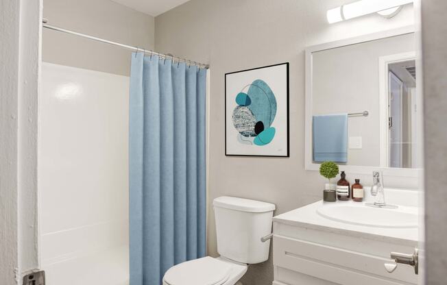 Two-Bedroom Apartments in Glendale, AZ - Spectra West - Bathroom with a Blue Shower Curtain, a White Shower and Bathtub, a Toilet, and a White Vanity