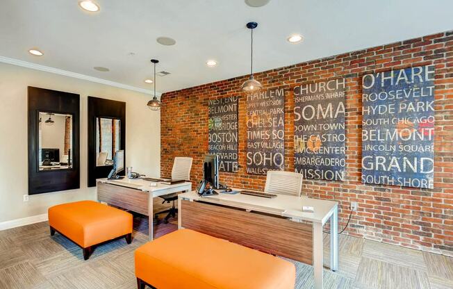 a brick wall in an office with two desks and orange chairs