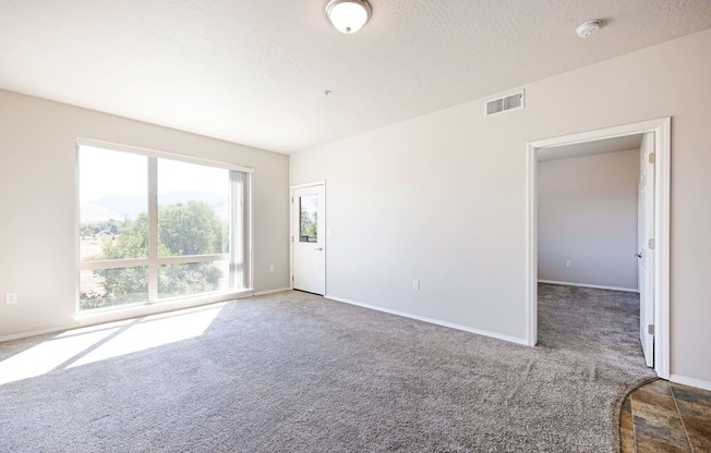 A spacious room with a carpeted floor and sliding glass doors leading to a balcony.