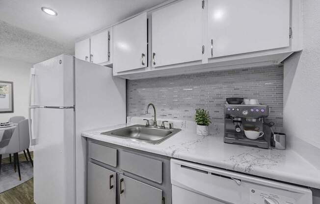 A modern kitchen with a white refrigerator, grey cabinets, and a marble countertop.