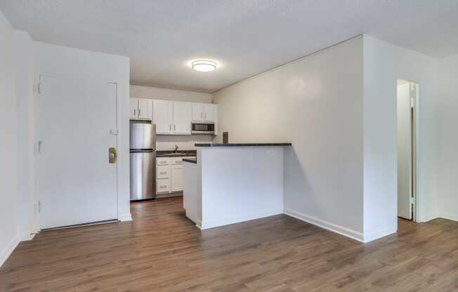 an empty living room with a kitchen in the background