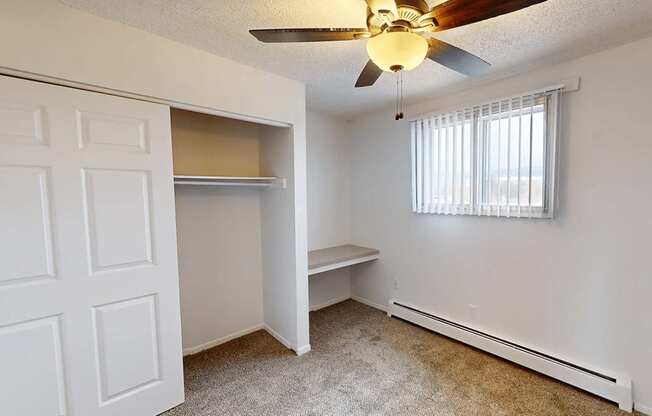 A room with a ceiling fan and a window with blinds.