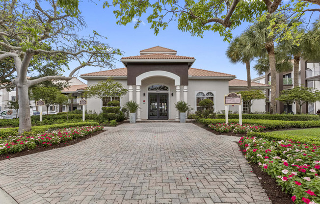 Exterior of leasing office and main building of property with cobblestone path and palm trees