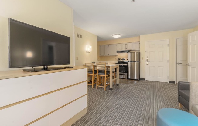 a living room with a television and a kitchen with a table and chairs