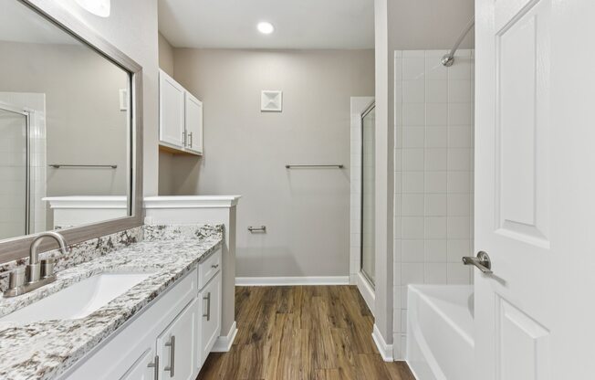A white bathroom with a marble counter top and wooden floors.