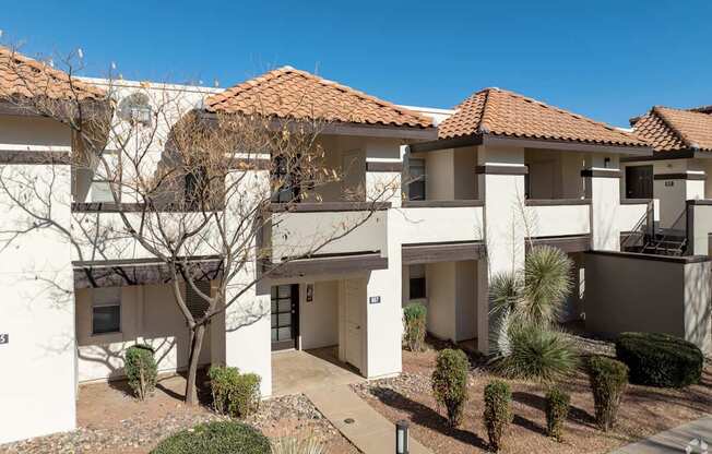 A white building with a red tile roof and a tree in front.