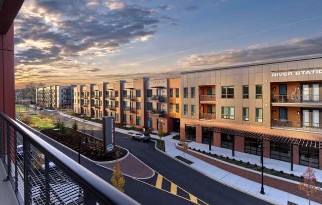 A balcony view of River Station's modern apartment building lining a street with the sun setting in the background.