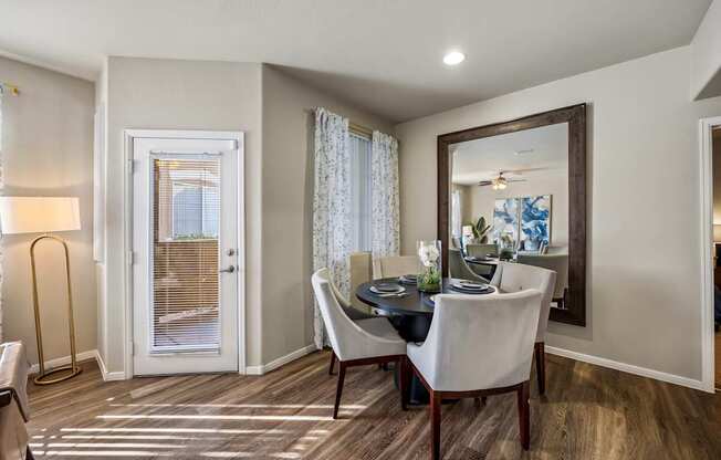 A dining room with a table set for two and a view of a door with blinds.