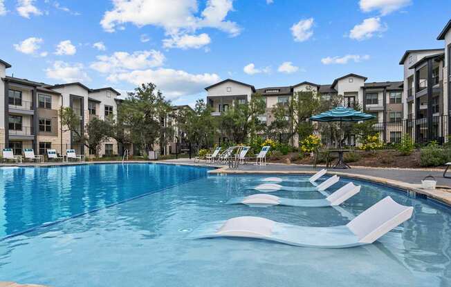 A swimming pool with lounge chairs and apartment buildings in the background.