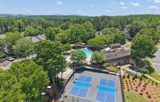 A tennis court surrounded by trees and a swimming pool.