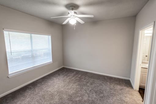 an empty bedroom with a ceiling fan and a window