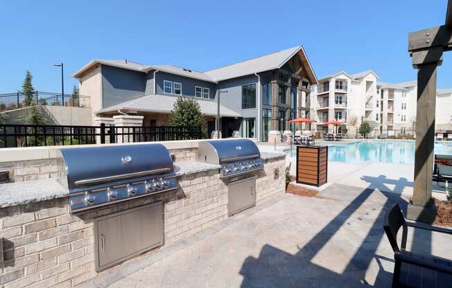 two bbq grills next to a pool with apartments in the background at The Crest at Acworth, Georgia