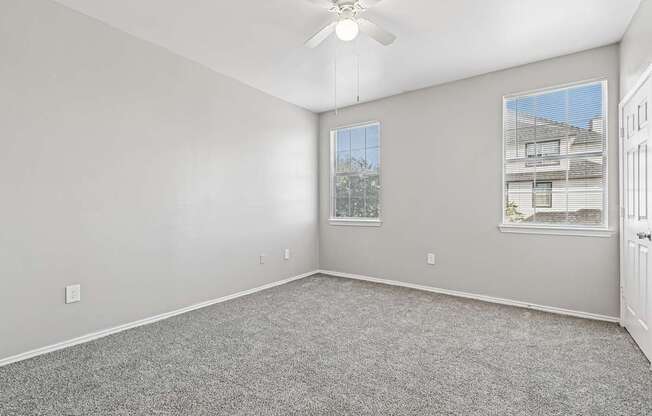 A room with a ceiling fan and two windows.