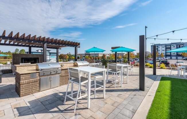 a patio with a grill and tables with chairs and umbrellas