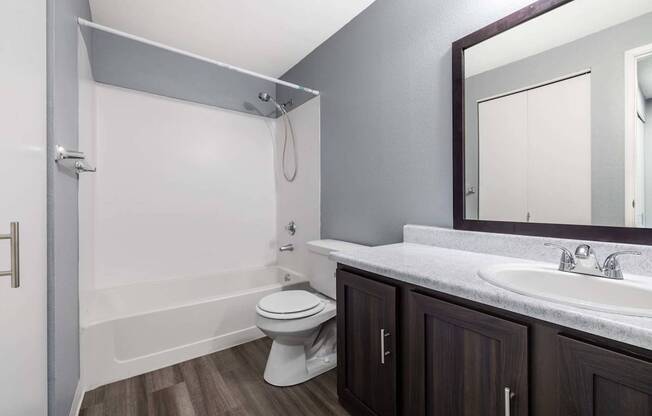 A white toilet sits in a bathroom with a white tub and a white sink.