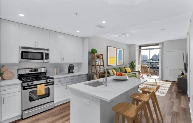 an open kitchen and living room with white cabinets and a marble counter top