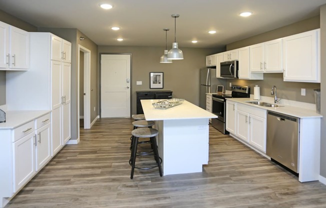A kitchen with white cabinets and a wooden floor. Fargo, ND 29 West Apartments
