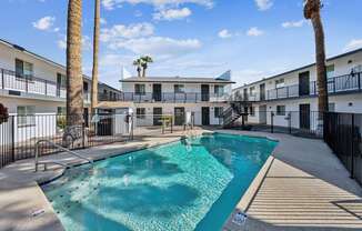 A swimming pool surrounded by palm trees and apartment buildings.