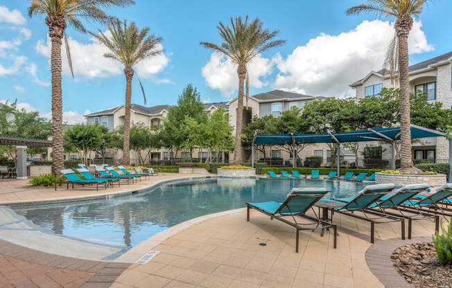 A pool surrounded by palm trees and lounge chairs.