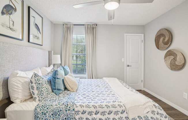 A bedroom with a bed, pillows, a ceiling fan, and a window with curtains.