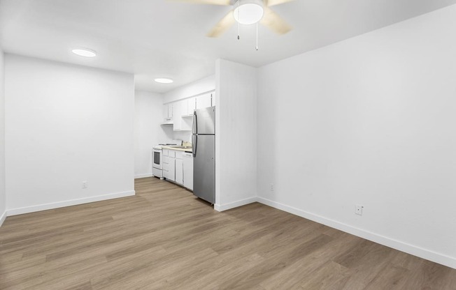 the living room and kitchen of an apartment with white walls and wood flooring