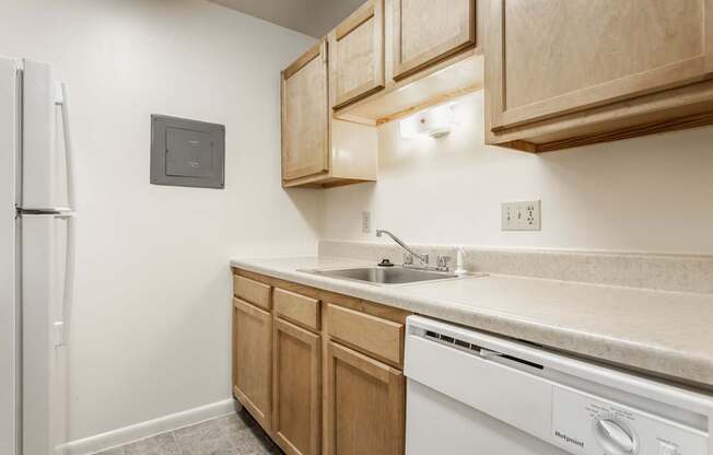A kitchen with a white fridge, wooden cabinets, and a white dishwasher.
