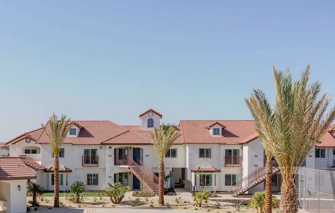A large white house with a red tile roof and palm trees in front.
