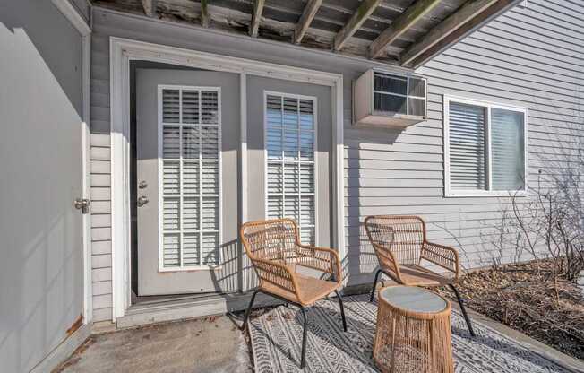 Two chairs and a table are on a porch.