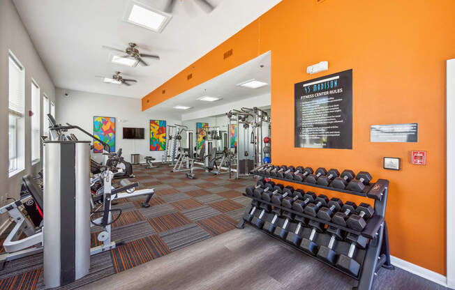 a spacious fitness center with cardio equipment and a colorful mural on the wall