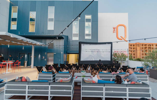 Pet-Friendly Apartments in Woodland Hills, CA - The Q Variel Apartments - Cinema Under the Stars Community Event On The Sunset Roof Deck with a Big Screen, Hanging Lights, and Cozy Seating