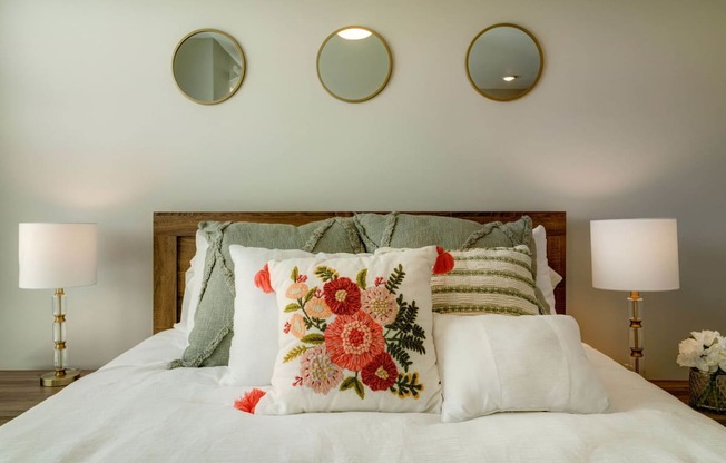 a bed with pillows and three mirrors on the wall above it